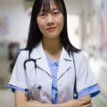 alt="Confident female doctor in medical uniform with stethoscope standing in hospital hallway
