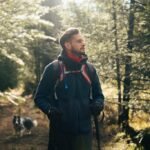 Man hiking with a backpack through a sunlit forest trail with a dog